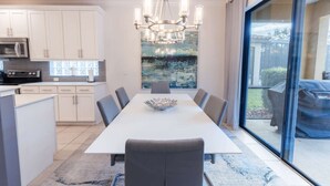 A modern kitchen with white cabinets, a large island, and a dining area with a long table and chairs. - Elsa's Enchanting Escape, just 15 minutes from Disney World! (Kissimmee)