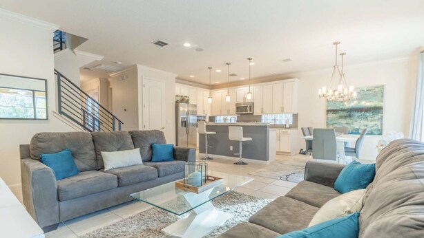 A modern living room with a grey sofa, a glass coffee table, and a dining area with a white table and chairs. - Elsa's Enchanting Escape, just 15 minutes from Disney World! (Kissimmee)