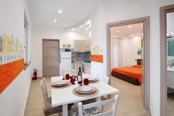 A compact hotel room with a dining area, kitchenette, and a bed with an orange bedspread.
