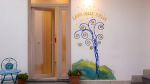 A hotel entrance with a glass door, a wall mural with a tree and text, and a blue chair with a potted plant. - Apartment 'Martina' with Mountain View, Wi-Fi and Air Conditioning (Agerola)