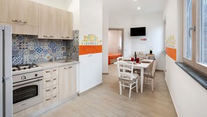 A modern kitchen with a gas stove, oven, and wooden cabinets. There is a dining area with a table and chairs, and a TV mounted on the wall. - Apartment 'Martina' with Mountain View, Wi-Fi and Air Conditioning (Agerola)