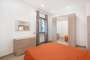 Une chambre à coucher comprenant un lit, une commode, un miroir, une fenêtre avec des rideaux et une armoire.