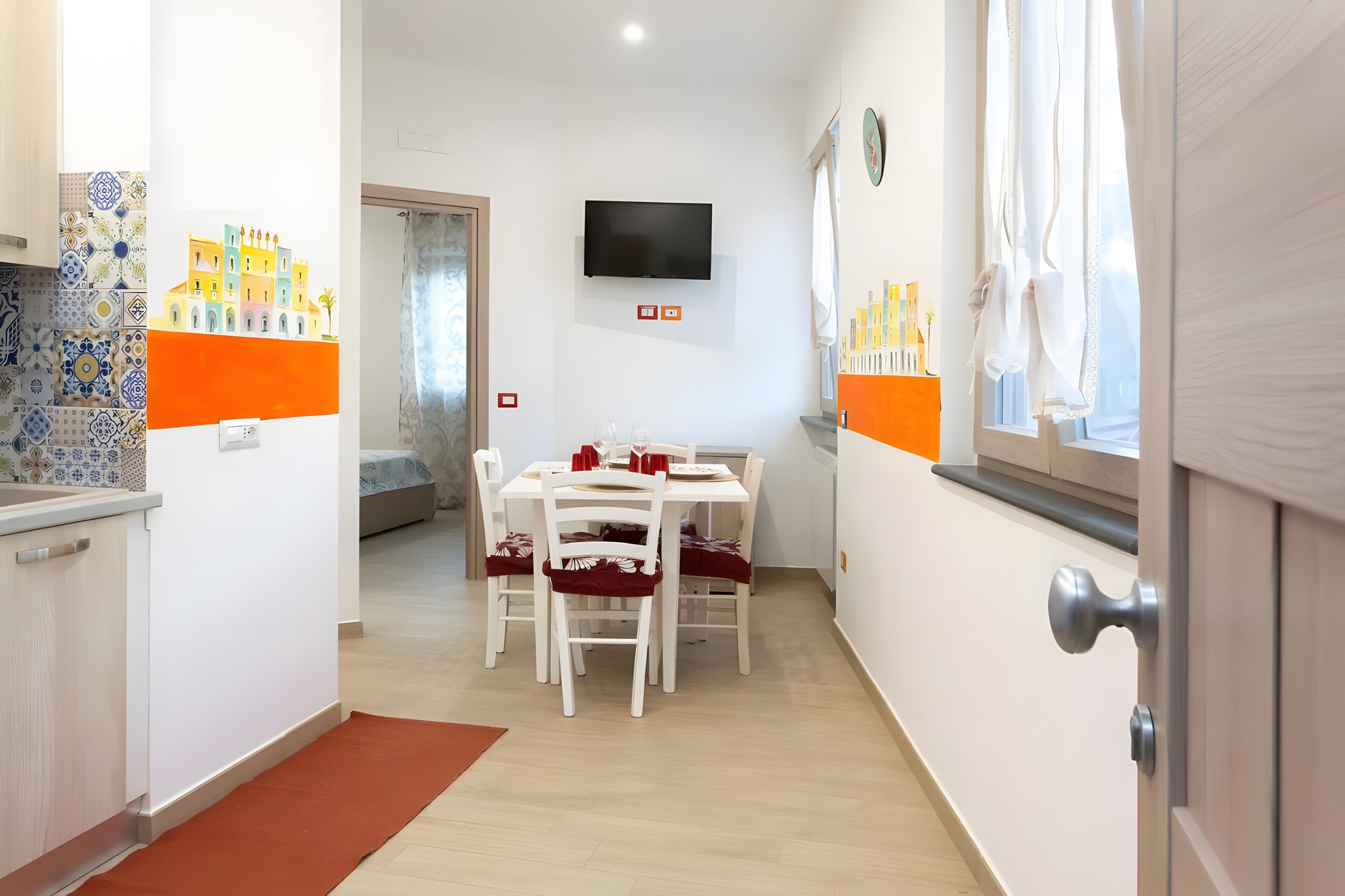 A narrow hallway with a dining area, a TV mounted on the wall, and a window with curtains.