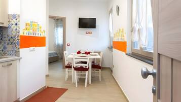 A narrow hallway with a dining area, a TV mounted on the wall, and a window with curtains.