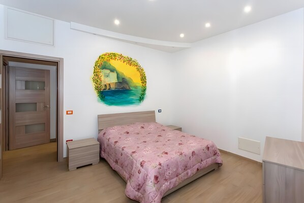A bedroom with a bed, a nightstand, a dresser, a door, and a wall with a painting.