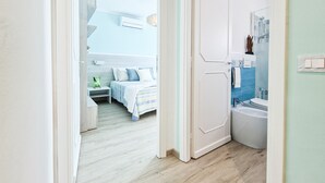 A hotel room with a bed, bedside table, and a bathroom with a sink and mirror.