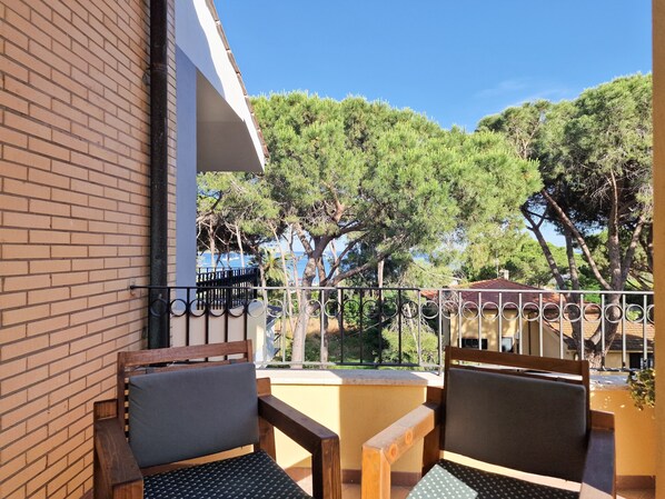 A balcony with two wooden chairs, a brick wall, and a view of trees and a body of water.