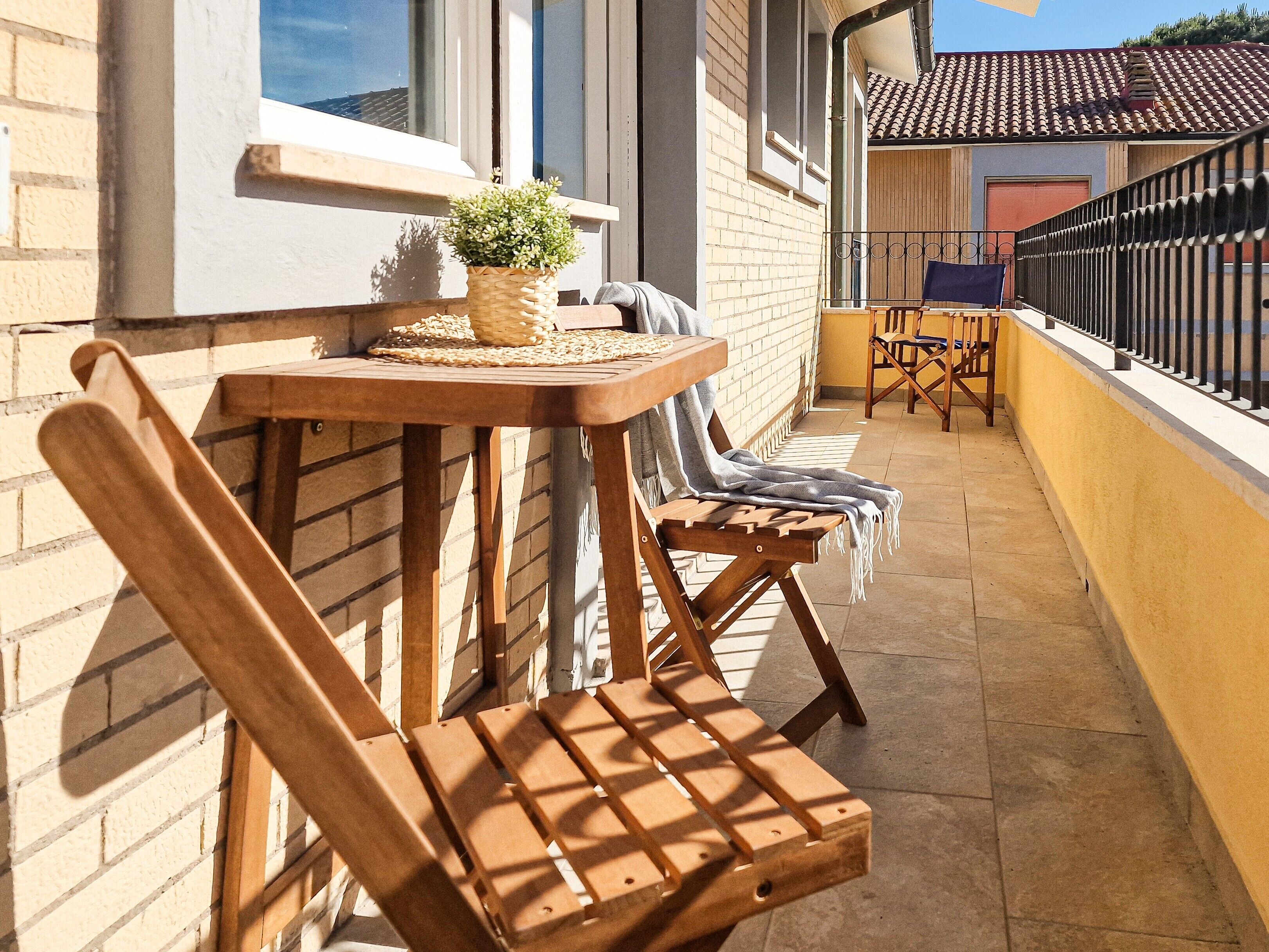 Un balcone con sedie in legno, un tavolino e una pianta in vaso.