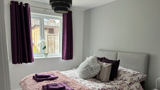 A bedroom with a bed, a window with curtains, a bedside table, and a nightstand. - Captivating 1-bed Apartment in Hednesford (Cannock)