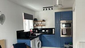A compact kitchen with a washing machine, a microwave, and a built-in oven. - Captivating 1-bed Apartment in Hednesford (Cannock)