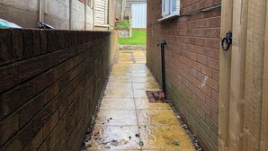 A narrow brick pathway leading to a gated area with a water spout on the right. - Captivating 1-bed Apartment in Hednesford (Cannock)