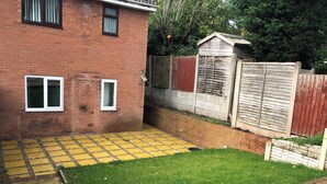 A backyard with a brick house, a wooden fence, and a small shed. - Captivating 1-bed Apartment in Hednesford (Cannock)