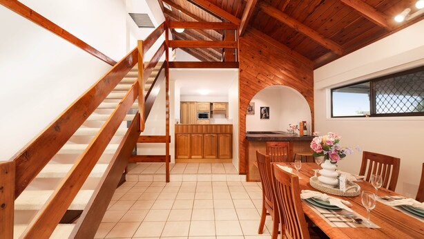 A wooden staircase leading to a kitchen with wooden cabinets and a dining area with a table set for two.