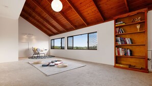 A spacious room with a high ceiling, a bookshelf, and a view through large windows.