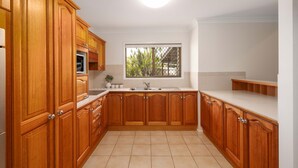 A kitchen with wooden cabinets, a white countertop, and a window with a view of greenery.