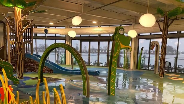 En inomhuslekplats med rutschkanor och klätterställningar, stora fönster och utsikt över vattnet utanför.