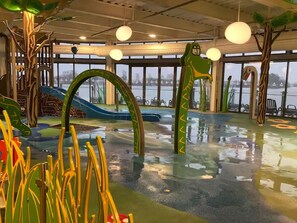 An indoor play area with slides and climbing structures, large windows, and a view of the water outside. - Caravan-sleep8-hottub-freep-balcony-familyfriendly (Lincoln)
