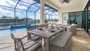 Un espace extérieur aménagé pour prendre les repas, avec vue sur une piscine et un ciel dégagé.