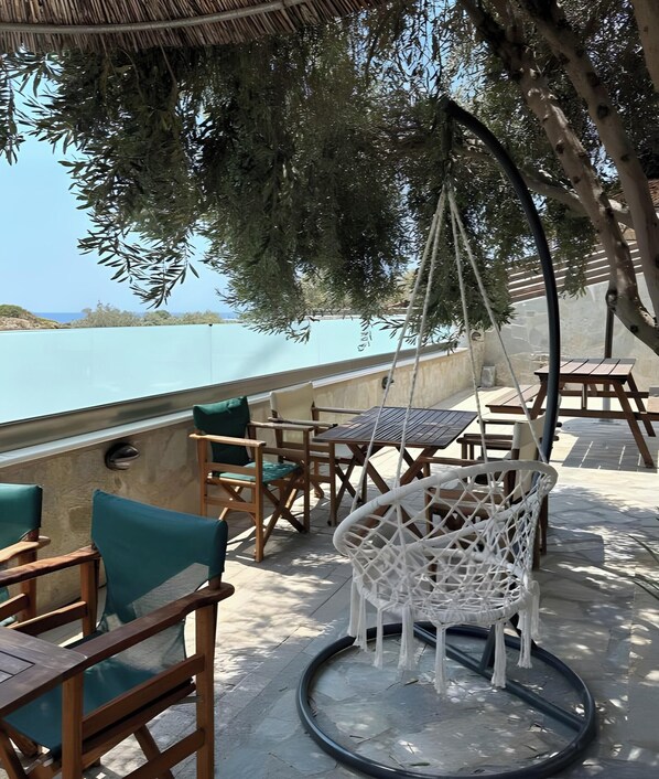An outdoor seating area with wooden furniture and a hanging chair, overlooking a body of water.