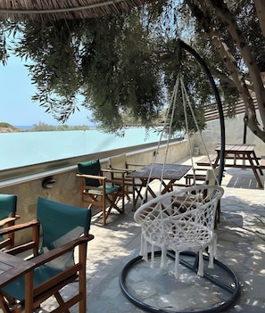 An outdoor seating area with wooden furniture and a hanging chair, overlooking a body of water.