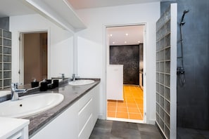 A modern bathroom with two sinks, a shower, and a tiled floor.