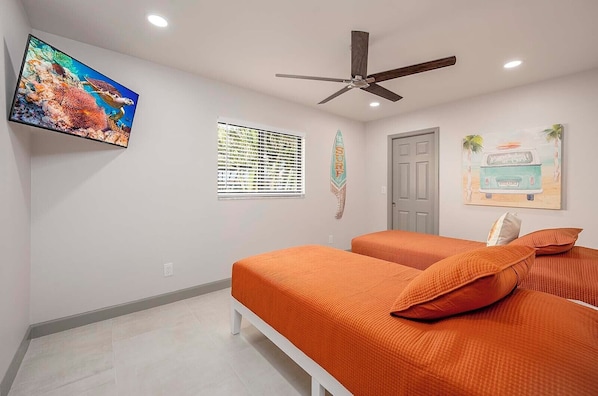 A bedroom with two beds, a ceiling fan, a TV, and wall decorations including a surfboard and a van.