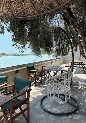 An outdoor seating area with wooden furniture and a hanging chair, overlooking a body of water.