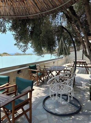 An outdoor seating area with wooden furniture and a hanging chair, overlooking a body of water.