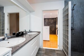 A modern bathroom with two sinks, a shower, and a tiled floor.
