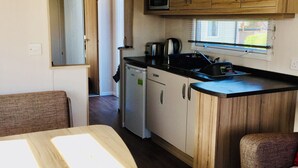 A compact kitchen with wooden cabinets, a microwave, a coffee maker, and a refrigerator. - Modern caravan, 5 mins walk to sandy beaches and South West coast path (Padstow)