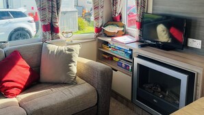 A cozy living area with a sofa, TV, and a bookshelf. - Modern caravan, 5 mins walk to sandy beaches and South West coast path (Padstow)