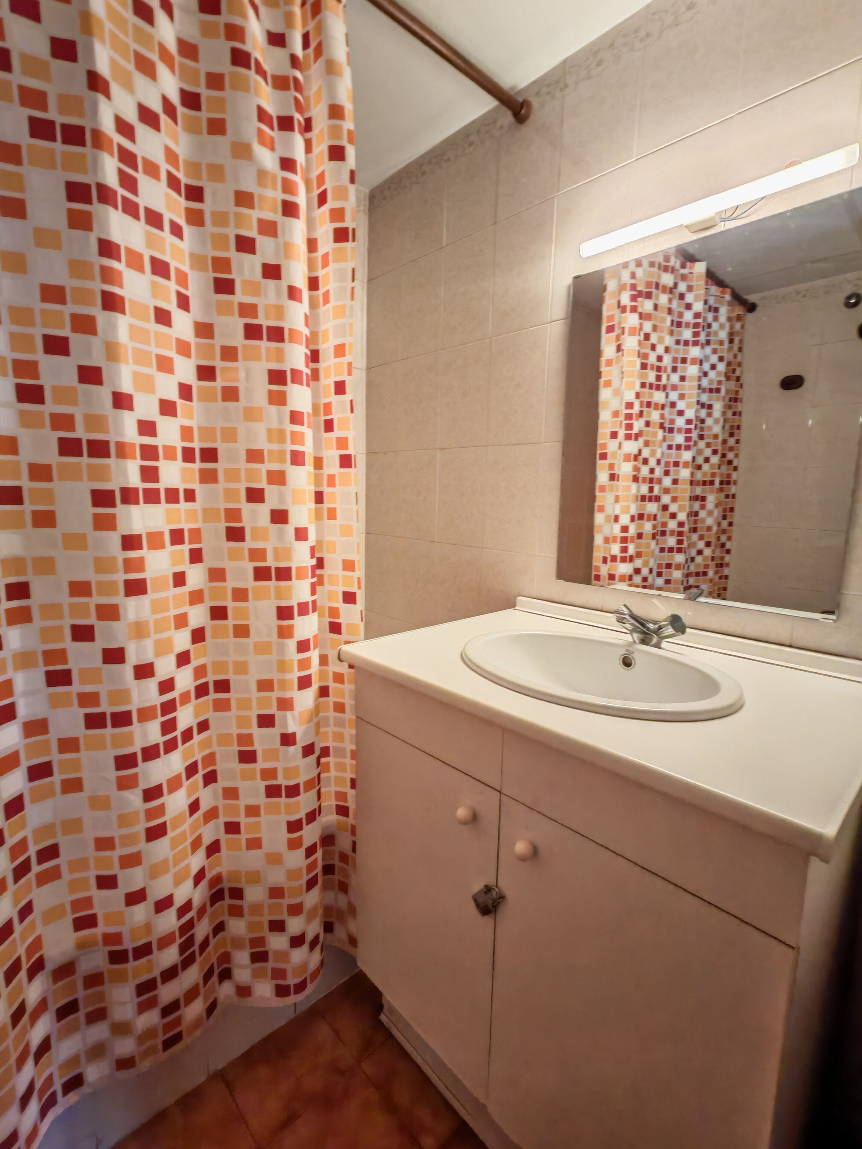 A bathroom with a tiled shower, a sink with a mirror, and a cabinet.