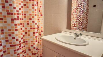 A bathroom with a tiled shower, a sink with a mirror, and a cabinet.