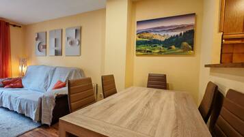 A cozy living room with a sofa, a dining table, and chairs. There is a painting on the wall and a lamp on the side.