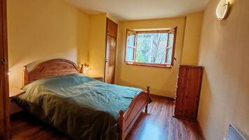 A bedroom with a wooden bed, a nightstand, a dresser, a window with a view of trees, and a radiator.