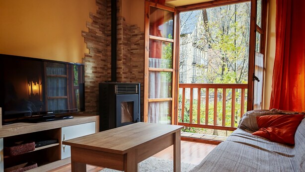 Una sala de estar acogedora con televisor, chimenea, sofá y un amplio ventanal con vista a árboles.