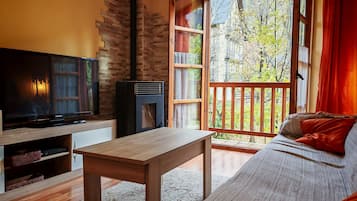 A cozy living room with a TV, a fireplace, a sofa, and a large window with a view of trees.