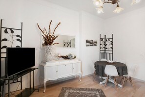 Uma sala de estar moderna com televisão de tela plana, armários brancos, uma mesa de jantar com cadeiras e objetos decorativos.