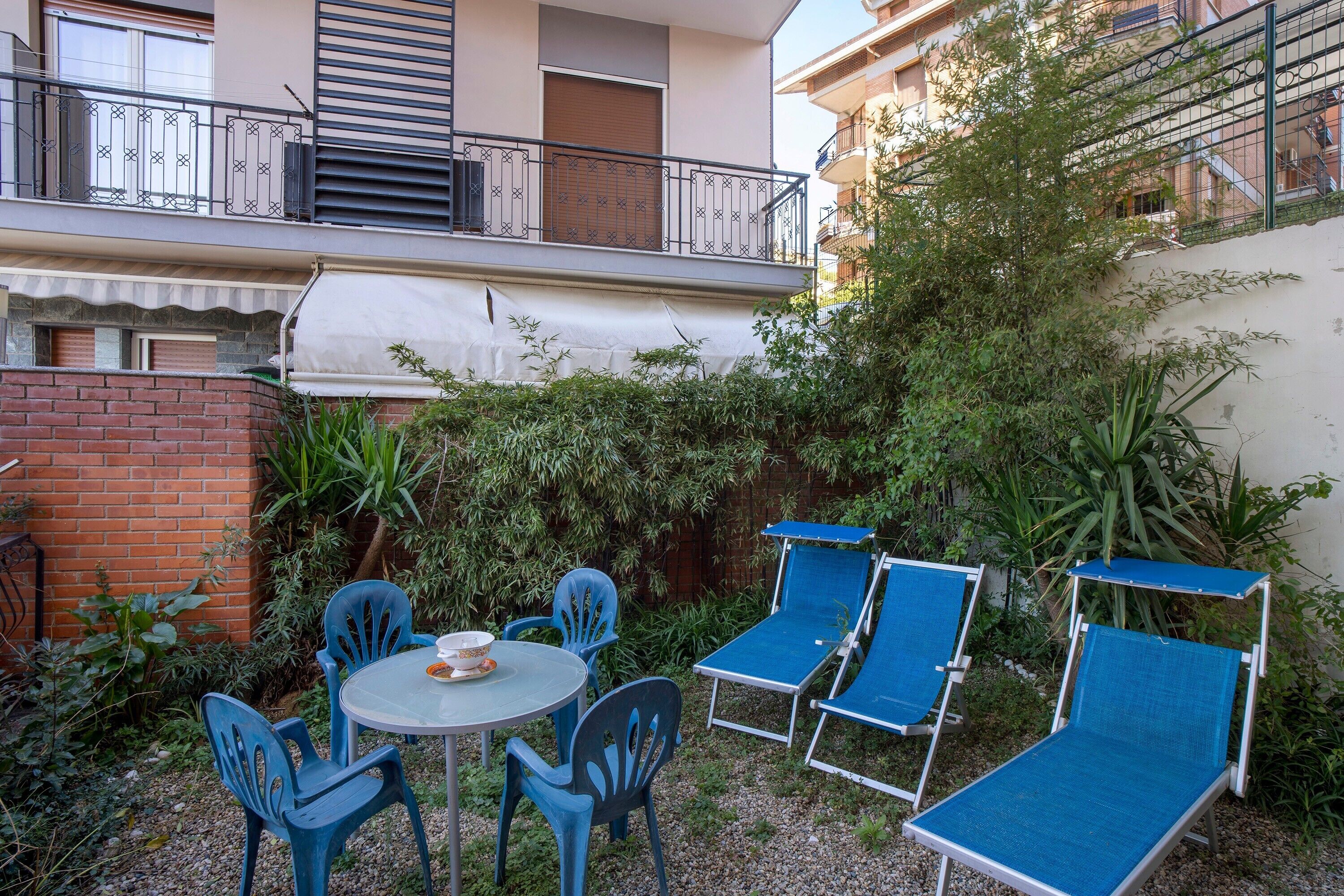 Un patio con un tavolo rotondo e quattro sedie, un tavolino con una ciotola e due poltrone blu.