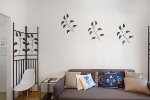 Una habitación con un sofá marrón, una silla blanca y decoración en la pared.