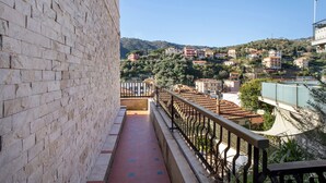 A balcony with a stone wall, a metal railing, and a view of a hillside with buildings. - Apartment 'Alassio Mare E Non Solo 2' with Sea View, Wi-Fi and Air Conditioning (Alassio)