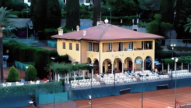 A yellow building with arched windows and a red roof, surrounded by greenery and a tennis court. - Apartment 'Alassio Mare E Non Solo 2' with Sea View, Wi-Fi and Air Conditioning (Alassio)