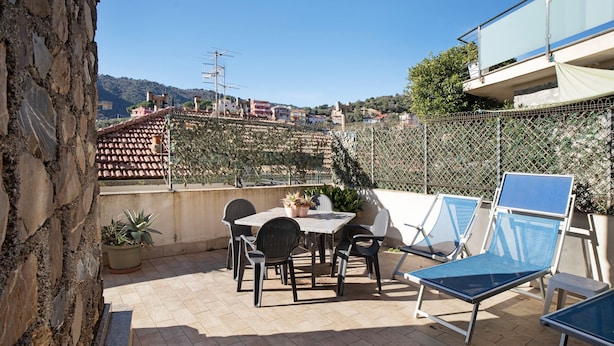 A patio with a table and chairs, a blue sun lounger, and a view of buildings and hills. - Apartment 'Alassio Mare E Non Solo' with Sea View, Wi-Fi and Air Conditioning (Alassio)