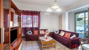A living room with a sofa set, a television, a wooden cabinet, and a table with a vase. - Apartment 'Alassio Mare E Non Solo' with Sea View, Wi-Fi and Air Conditioning (Alassio)