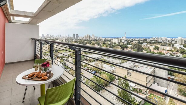 Ein Balkon mit Frühstückstisch, der auf einen Blick über die Stadt mit Gebäuden und einem klaren Himmel bietet.