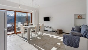 Un salon moderne comprenant un coin repas, un canapé, un téléviseur fixé au mur et une vue sur les montagnes grâce à de grandes fenêtres.