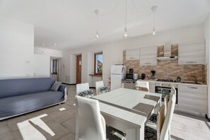 Una sala moderna con sofá, mesa de comedor y sillas, una cocina equipada, y vistas al exterior.