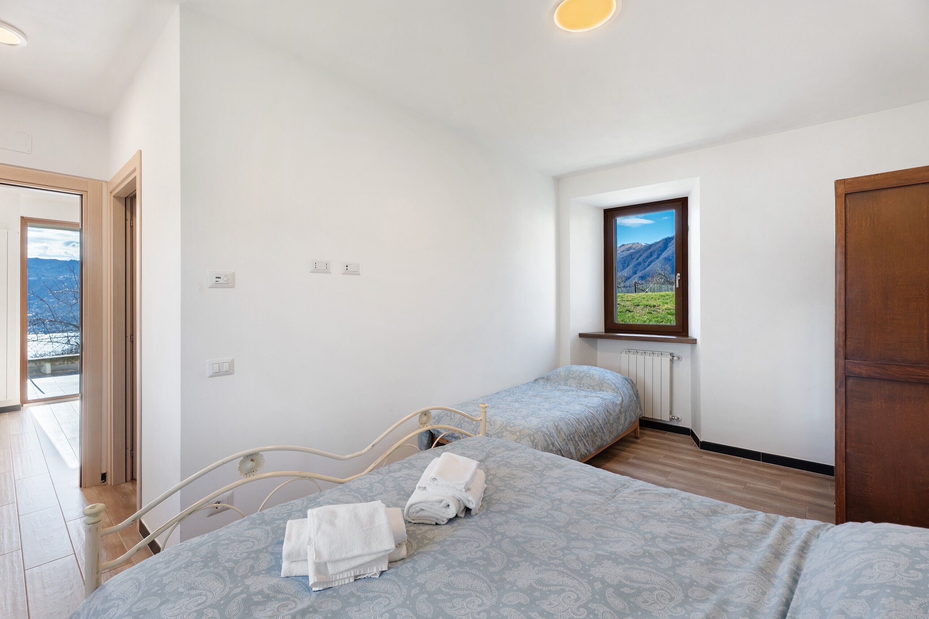 A bedroom with two beds, a window with a mountain view, and a door.