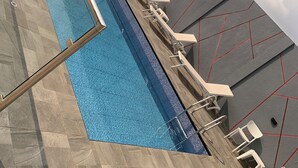 Una piscina con suelo de baldosas, una escalera y sillas blancas.