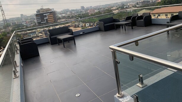 Terraza en la azotea con mobiliario exterior, barandilla de cristal y vistas a la ciudad.